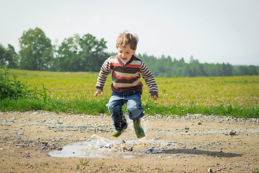 pexels-photo-1104014-1104014 A cheerful child in a striped sweater jumps into a puddle on a sunny day in Czechia.