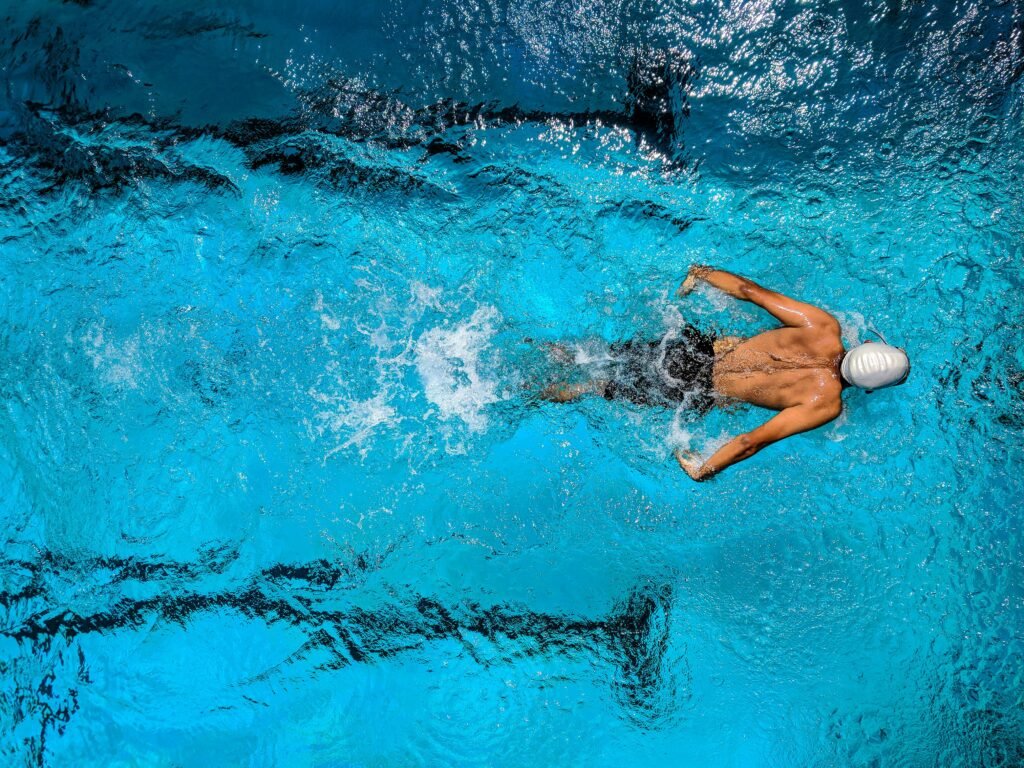 pexels-photo-863988-863988 Top view of a swimmer wearing a cap, performing a front crawl stroke in a clear blue swimming pool.